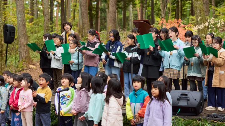 緑の楽譜を持った子どもたちが、ステージの上と前に並んで合唱している。