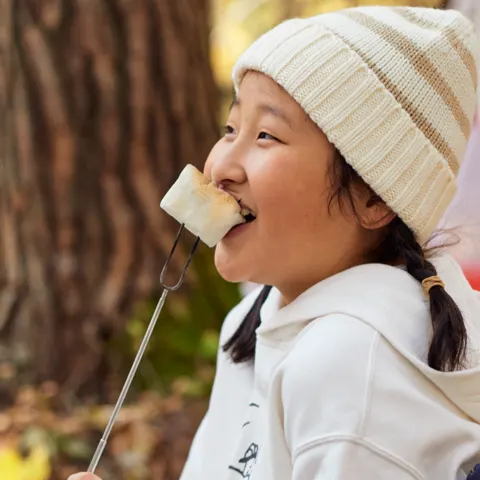 白いニット帽の女の子が、串に刺したおやつを口にくわえて、声を出して笑っている。